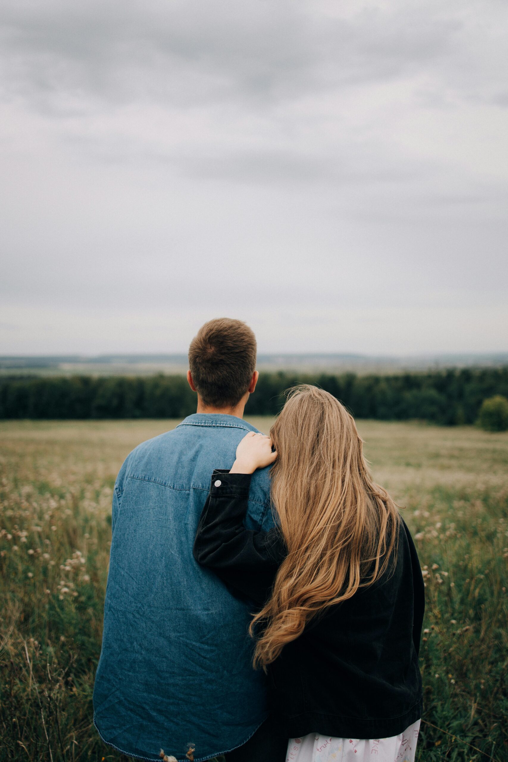 A couple shares an intimate moment in a grassy field under a cloudy sky.