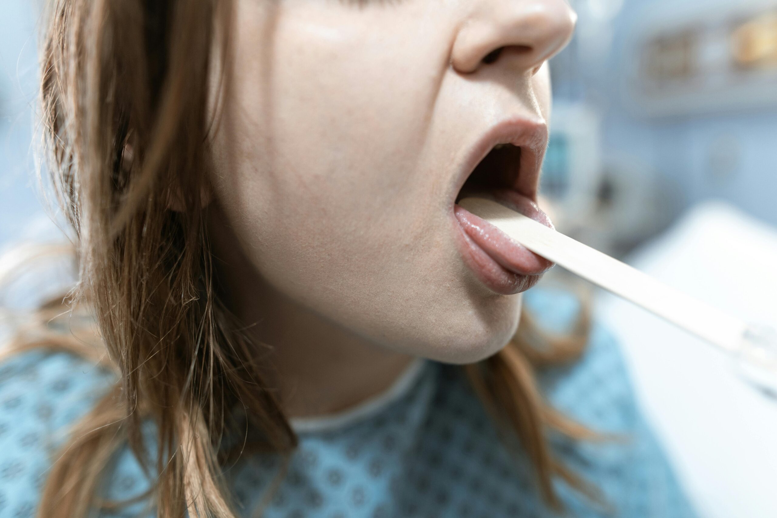 Close-up of a woman having her throat examined in a medical setting with a tongue depressor.