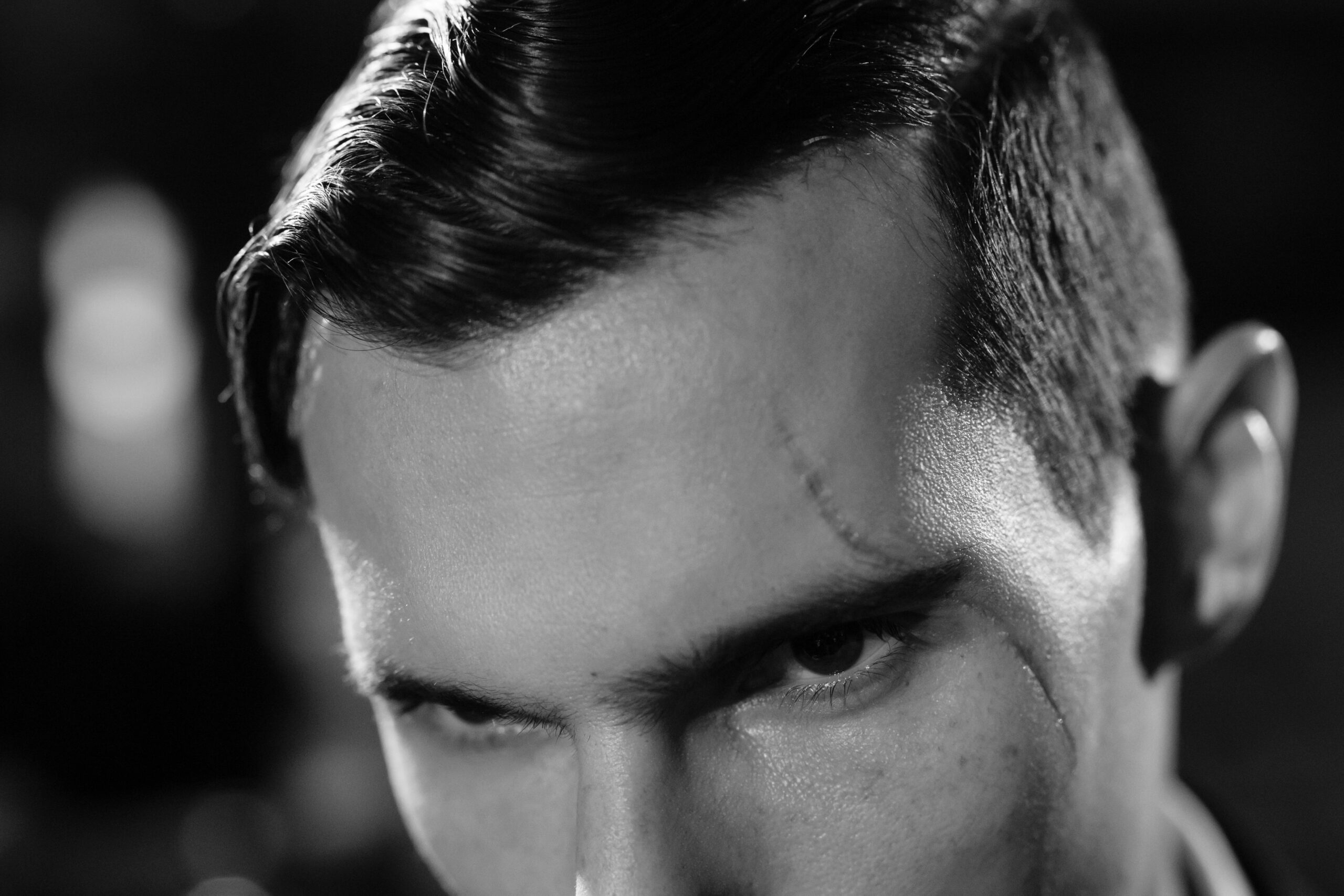 Close-up black and white portrait highlighting a scarred face with a moody, cinematic atmosphere.